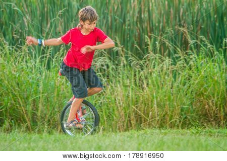outdoor portrait of young boy riding a unicycle (one wheel bike) on natural background