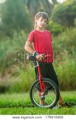 outdoor portrait of young boy riding a unicycle (one wheel bike) on natural background