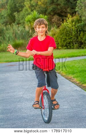 outdoor portrait of young boy riding a unicycle (one wheel bike) on natural background