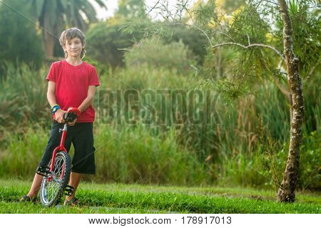 outdoor portrait of young boy riding a unicycle (one wheel bike) on natural background