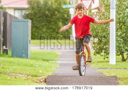 outdoor portrait of young boy riding a unicycle (one wheel bike) on natural background