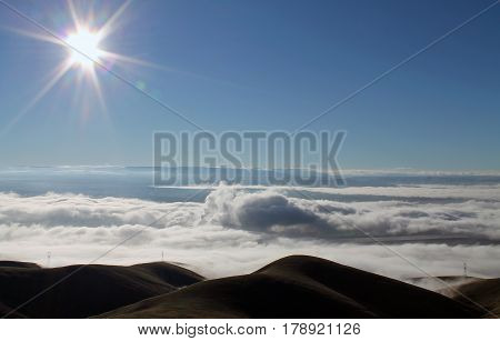 Clouds Covering a Mountain Valley at Sunrise with Sunburst in a Blue Sky
