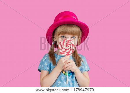 Funny child with candy lollipop, happy little girl eating big sugar lollipop, kid eat sweets. surprised child with candy. isolated on bright background, studio. Beautiful little girl with lollipop