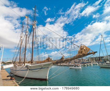 Tall sailing ship at Marina Port Vell in Barcelona, Spain.  Sailboats and pleasure craft in harbor on a warm November afternoon.