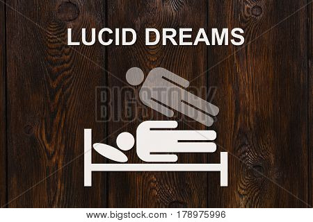 Paper sleeping man on bed with text LUCID DREAMS on wooden background. Abstract conceptual image