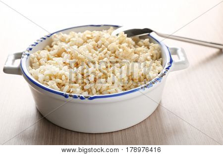 Modern ceramic saucepan full of boiled brown rice on wooden table