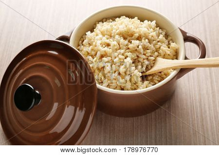 Modern ceramic saucepan full of boiled brown rice on wooden table