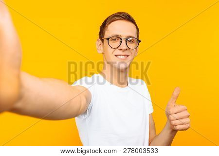 Man In Glasses And White T-shirt Showing Thumbs Up Taking A Selfie On Yellow Background