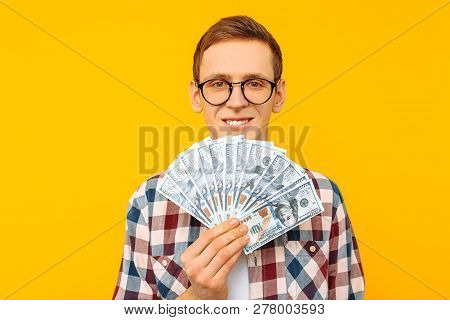 Happy Man In Glasses And A Plaid Shirt, With Dollar Bills, On Yellow Background