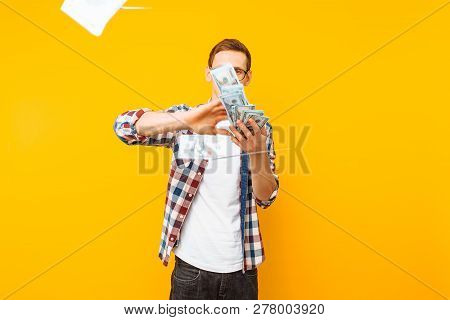 Happy Man, Wearing Glasses And A Plaid Shirt, Throwing Out Money Banknotes On A Yellow Background