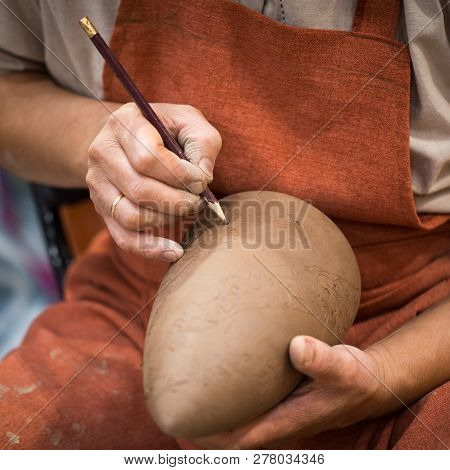 Ceramic Workshop, The Master Puts Otnament On Unfired Earthenware Jug. Close-up Of Master Hands. Mad