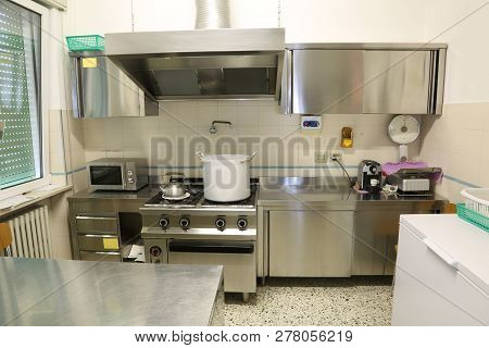 Interior Of An Industrial Kitchen With A Large Hood And A Giant Metal Pot On The Stove And A Steel T