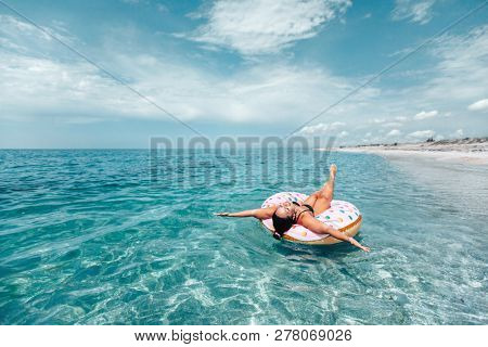 Plus size woman chilling on lilo in the sea water. Girl relaxing on inflatable ring on the beach. Summer vacations, idyllic scene.