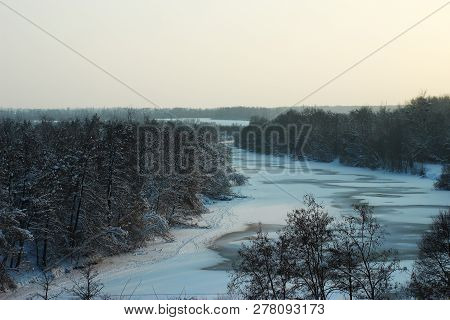 Winter Landscape With Frozen River. On The Sides Of The Hills Covered With Trees.