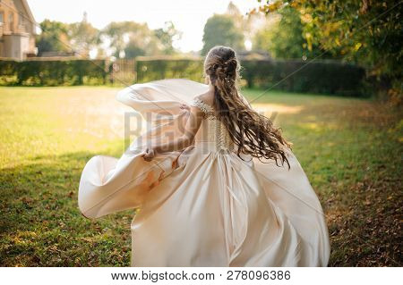 Back View Of A Beautiful Bride Spinning In A Wedding Dress Dancing On The Green Field