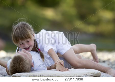 Two Young Happy Cute Blond Laughing Children, Boy And Girl, Brother And Sister Having Fun On Pebbled
