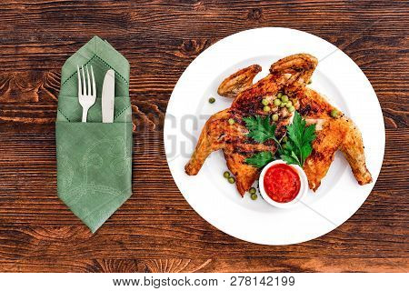Grilled Fried Roast Chicken Tabaka On A Plate On A Wooden Background, Top View With Appliances