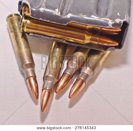 A Loaded Ar-15 Rifle Magazine On Top Of Four .223 Caliber Bullets On A White Background