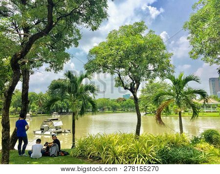 Lumpini Park, Bangkok, Thailand - May 18th, 2017: A Group Of Locals Relaxing Under The Shade Of A Tr