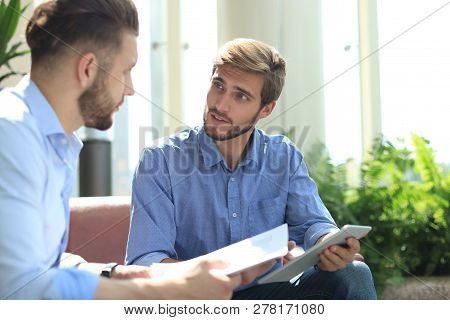 Mature Businessman Using A Digital Tablet To Discuss Information With A Younger Colleague In A Moder