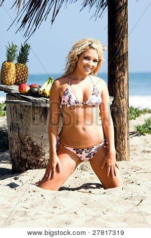Ragazza bionda sexy del bikini in spiaggia in bikini rosa e marrone di Swimbay sotto un ombrello palapus w