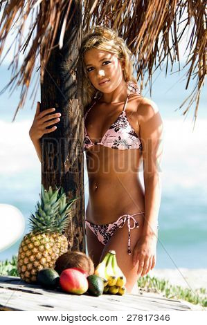 Ragazza bionda sexy del bikini in spiaggia in bikini rosa e marrone di Swimbay sotto un ombrello palapus w