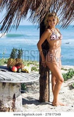 Ragazza bionda sexy del bikini in spiaggia in bikini rosa e marrone di Swimbay sotto un ombrello palapus w