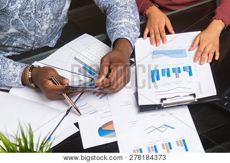 Hands Of Black People Holding Mobile Phone On Background Of Financial Documents In Business Space Cl