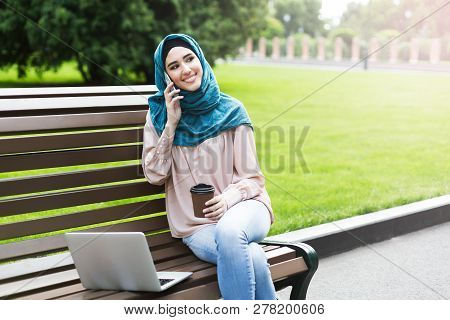 Smiling Muslim Women With Hijab Talking By Phone Using Laptop, Having Coffe Breakin Park. Always In 