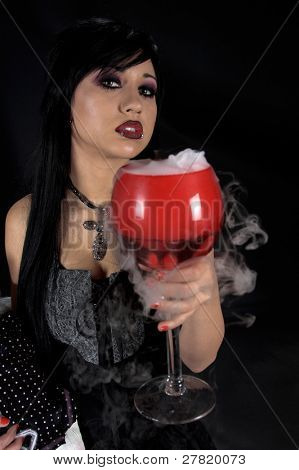Güzel kuzgun saçlı Gotik vampir kız witche bir kadeh ile oturan siyah ve gri elbise