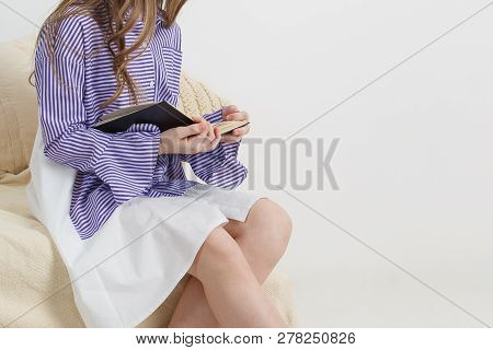 Girl In A Striped Dress Sits And Reads A Book On The Couch