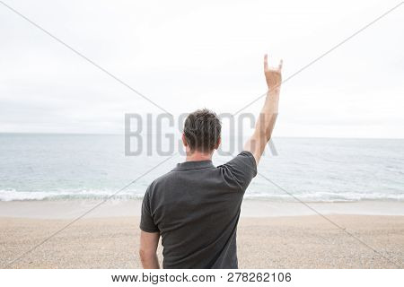 A Rear View Of A Strong Young Man Raising His Arm In Teh Air And Giving A Devil Horn Gesture Whilst 