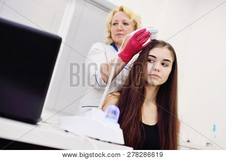 Doctor Dermatologist Diagnoses The Structure Of The Hair Of A Young Pretty Girl With A Special Tool 