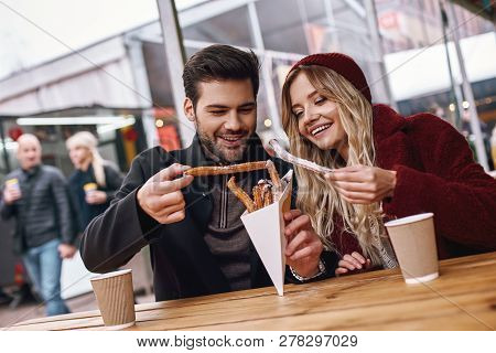 Close-up Of Young Couple Are Eating Churros At The Street Food Market.