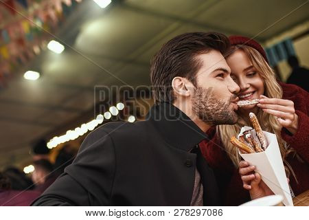 Close-up Of Young Couple Are Eating Churros At The Street Food Market.
