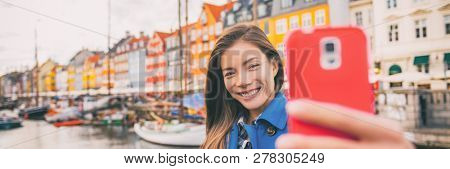 Selfie tourist girl taking photo with phone at Copenhagen Nyhavn, famous Europe tourism attraction. Asian woman at waterfront water canal in Kobenhavn, Denmark, Scandinavia. Banner panorama.
