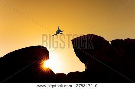 Challenge, Risk And Freedom Concept. Silhouette A Man Jumping Over Precipice Crossing Cliff