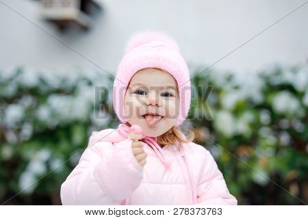 Portrait Of Little Toddler Girl Walking Outdoors In Winter. Cute Toddler Eating Sweet Lollypop Candy