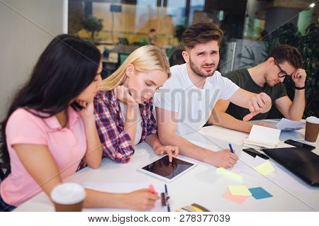 Unhappy And Upset Young Man Hold Big Thumb Down. He Is Dissapointed. Another People In Team Works. T