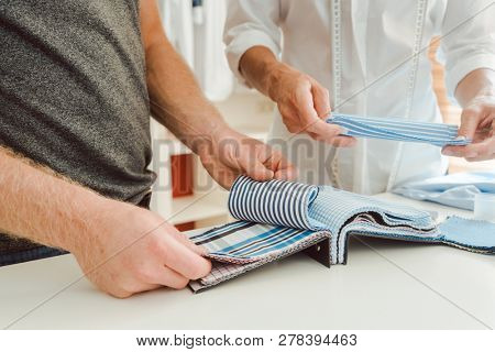Tailor and customer choosing material for bespoke shirt from pattern book