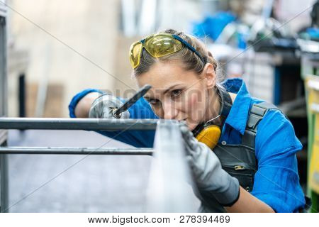 Woman metalworker checking the accuracy of her work holding steel file in her hand
