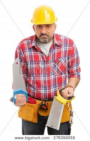 Builder Holding Two Blue And Yellow Sawa With Confused Expression Isolated On White Studio Backgroun