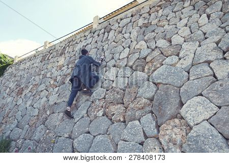 Caucasian Young Man Climbing On A Stone Wall In Banyalbufar Majorca. Selective Focus