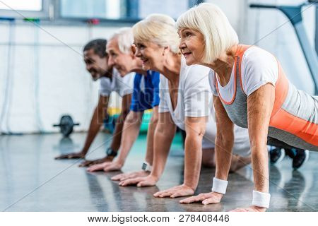 Side View Of Mutiethnic Senior Athletes Doing Plank At Sports Hall