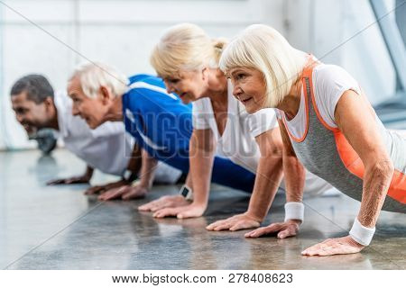 Cheerful Mutiethnic Senior Athletes Doing Plank At Sports Hall