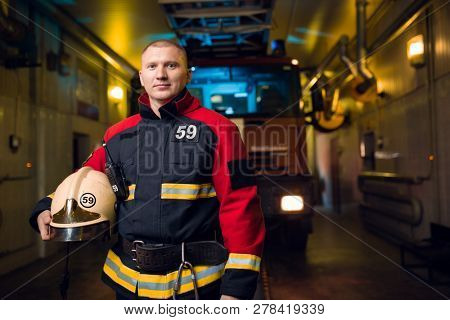 Photo of fireman holding helmet in hands on background of fire truck