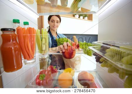 Portrait of female standing near open fridge full of healthy food, vegetables and fruits. Portrait of female