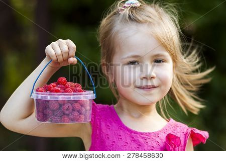 Portrait Of A Little Girl Child Holdind Small Basket Of Ripe Raspberries. Close-up