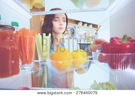 Portrait of female standing near open fridge full of healthy food, vegetables and fruits. Portrait of female