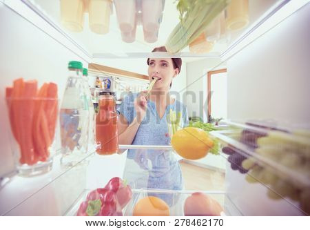 Portrait of female standing near open fridge full of healthy food, vegetables and fruits. Portrait of female
